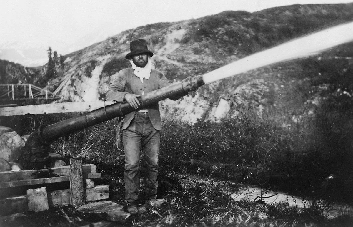 Historic gold miner operating water cannon at mining site in black and white photograph