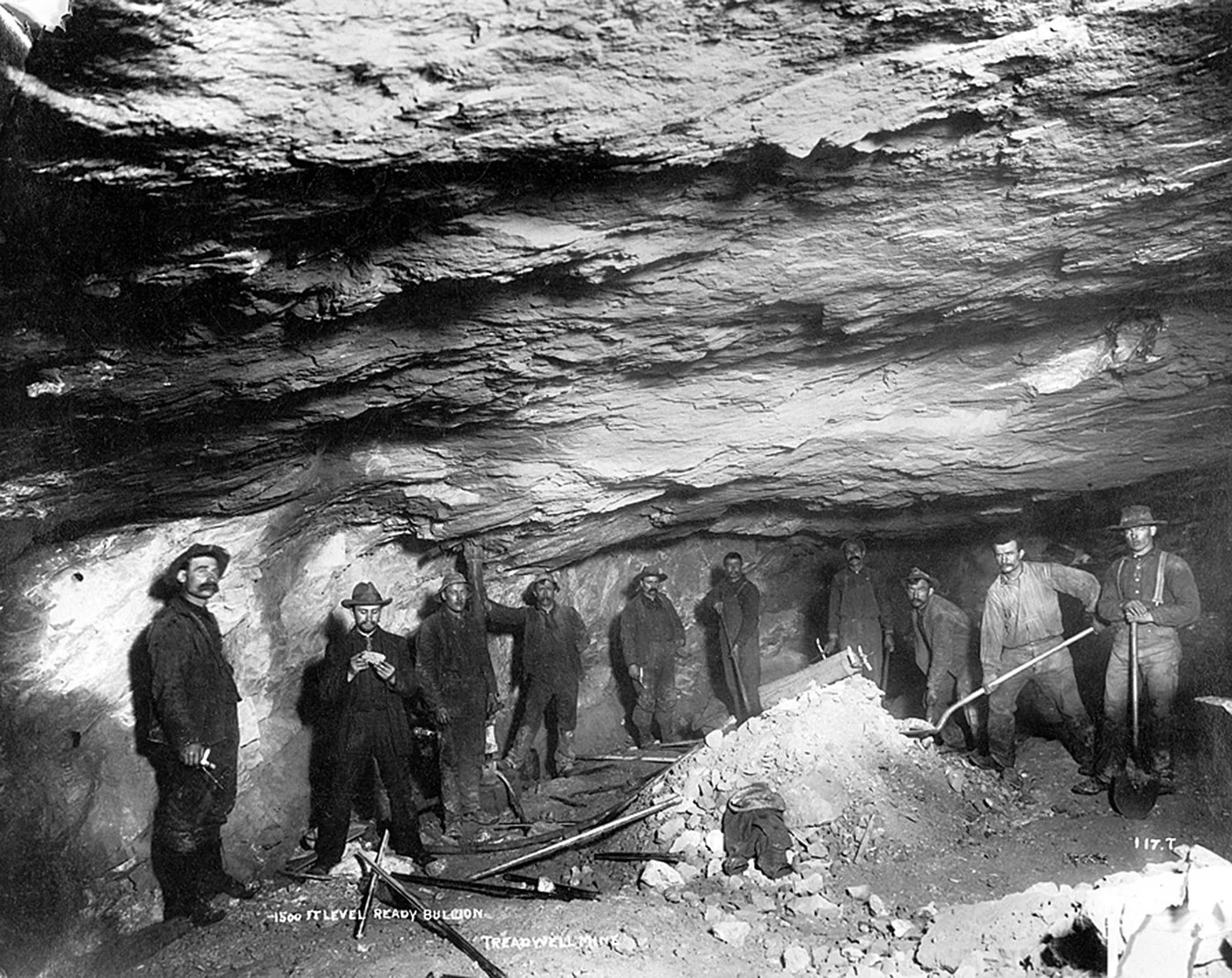 Group of miners standing inside underground mine tunnel with tools and excavated rock