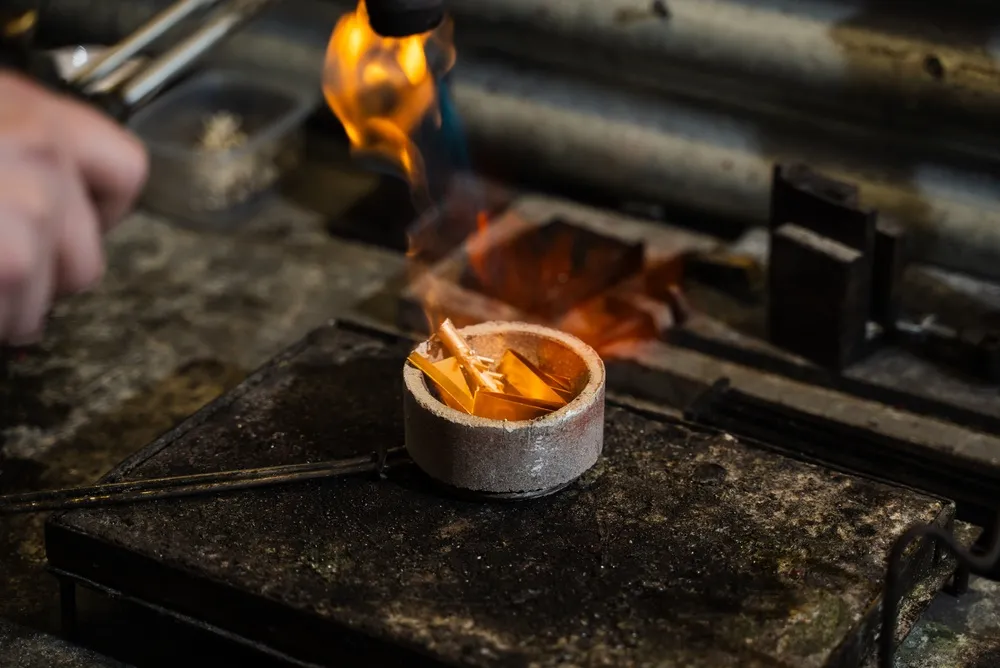 A person carefully ignites kindling in a metal bowl to start a fire outdoors.